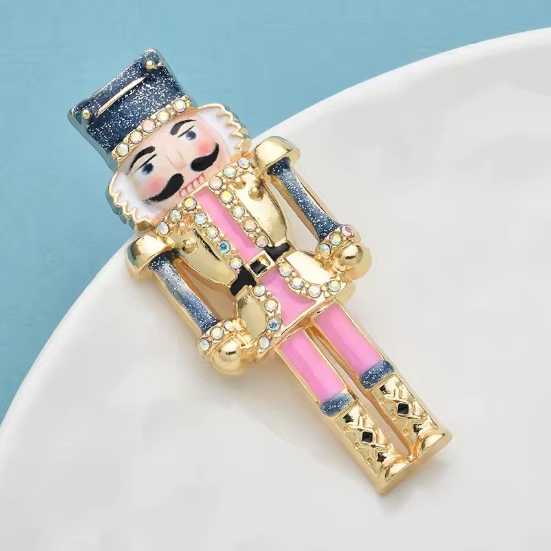 Nussknacker Soldat Brosche liegend auf Teller blauer Hintergrund