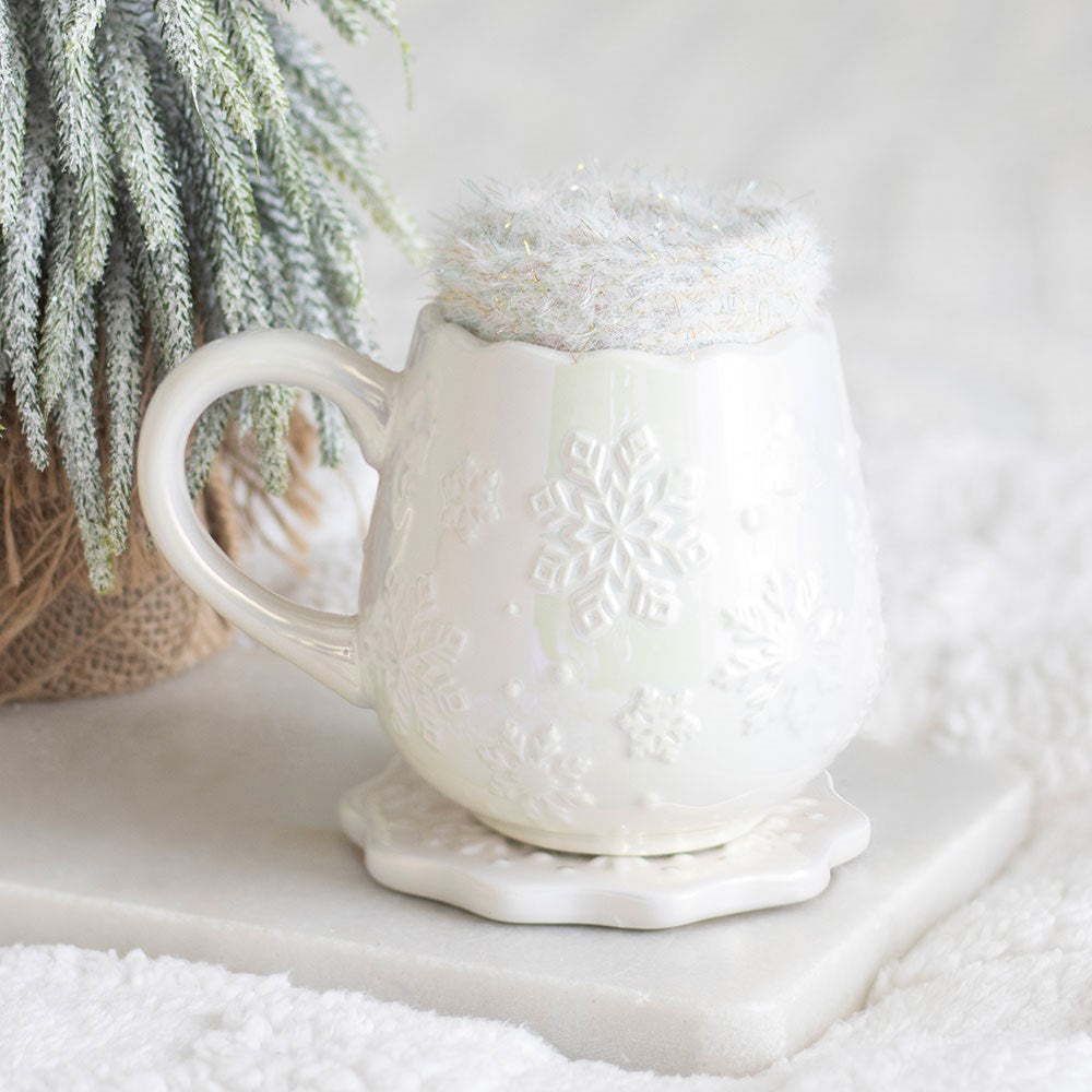 Schneeflocken Keramiktasse Perlmutt Weiß – Lifestyle mit Flauschsocken-Topper auf Untersetzer, Winterzweig im Hintergrund